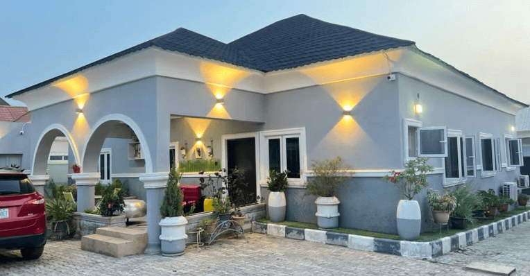 A newly built single-storey family home at dusk, with exterior wall lights on.